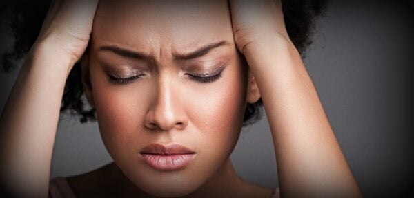 A woman holds her head with her eyes closed.