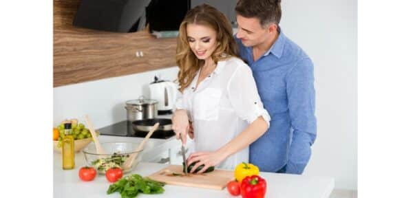 a couple together in the kitchen and the women cutting up vegetables for a salad